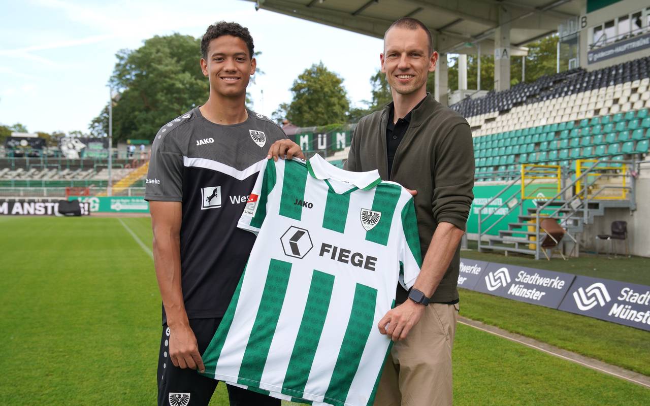 András Németh steht in einem grauen Trikot auf der linken Seite des Bildes. Ole Kittner steht neben ihm. In ihrer Mitte halten sie das weiß-grün gestreifte Trikot des SC Preußen Münster.