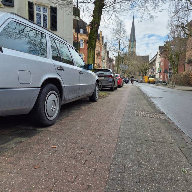 Auf dem Gehweg an einer Straße steht ein geparktes Auto. Daneben ist nur noch wenig Platz für einen Radstreifen. Vom Gehweg selbst ist nichts zu sehen.