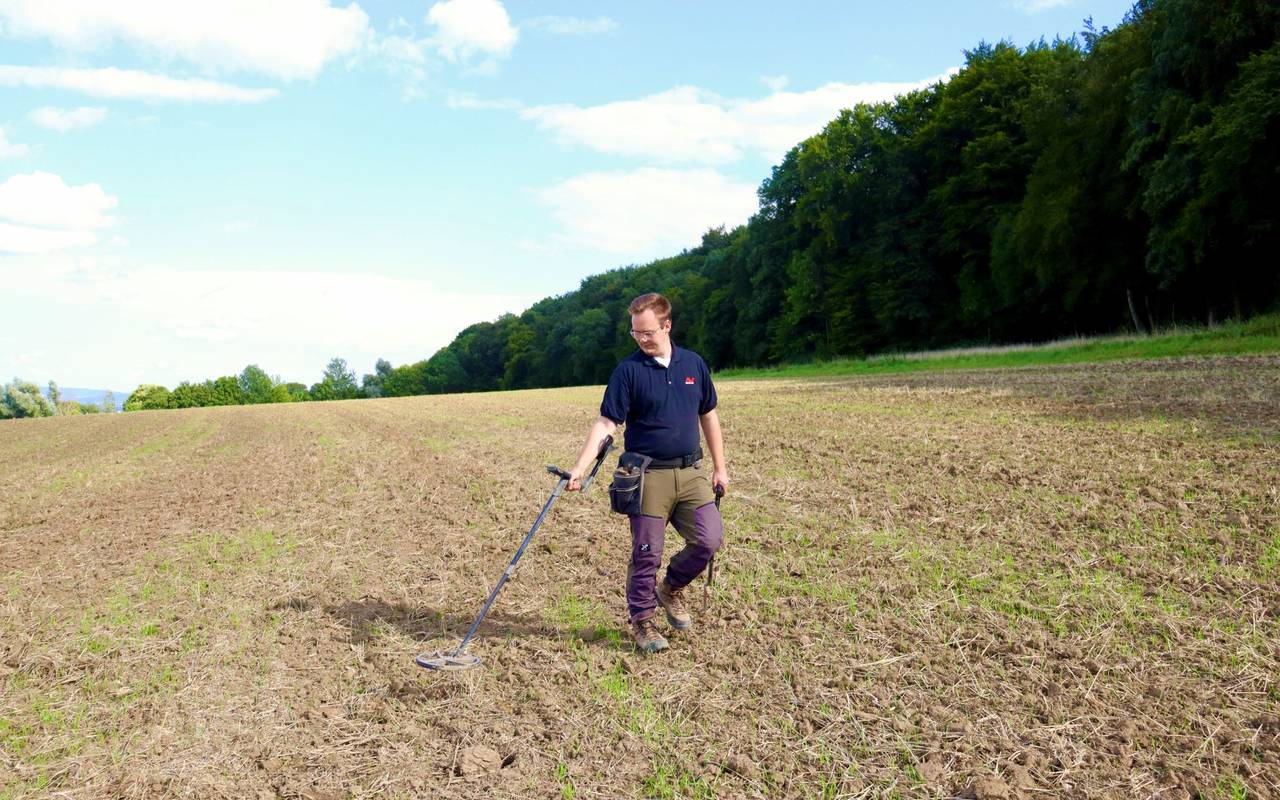 Ein Mann mit einem Metalldetektor auf einem Acker.