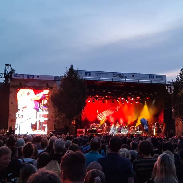 Eine Menge von Menschen steht mit dem Blick in Richtung einer Bühne. Die Bühne ist rot beleuchtet.