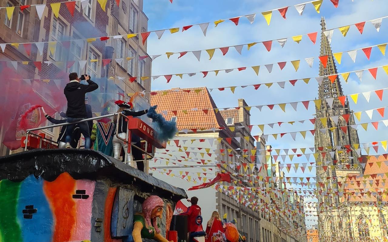 Ein Foto vom Münsteraner Prinzipalmarkt an Rosenmontag. Viele verkleidete Menschen bejubeln einen bunten Karnevalswagen.