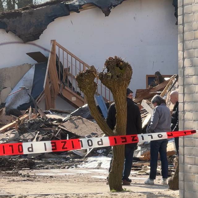 Hinter einem weiß-roten Flatterband sieht man Trümmer eines Gebäudes.