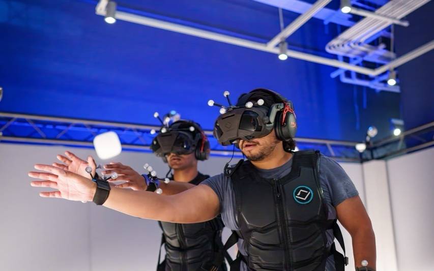 Zwei Menschen tragen eine große Virtual-Reality-Brille und schwarze Westen.