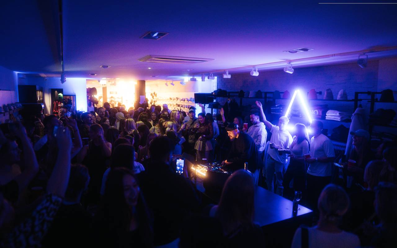 In einem kleinen Verkaufsraum feiern mehrere Menschen im dunklen Disco-Licht.