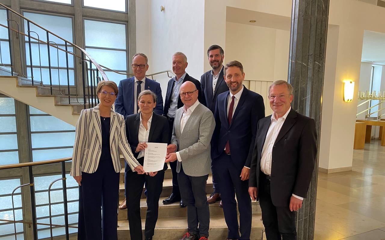 Acht erwachsene Menschen zeigen ein wichtiges Stück Papier.