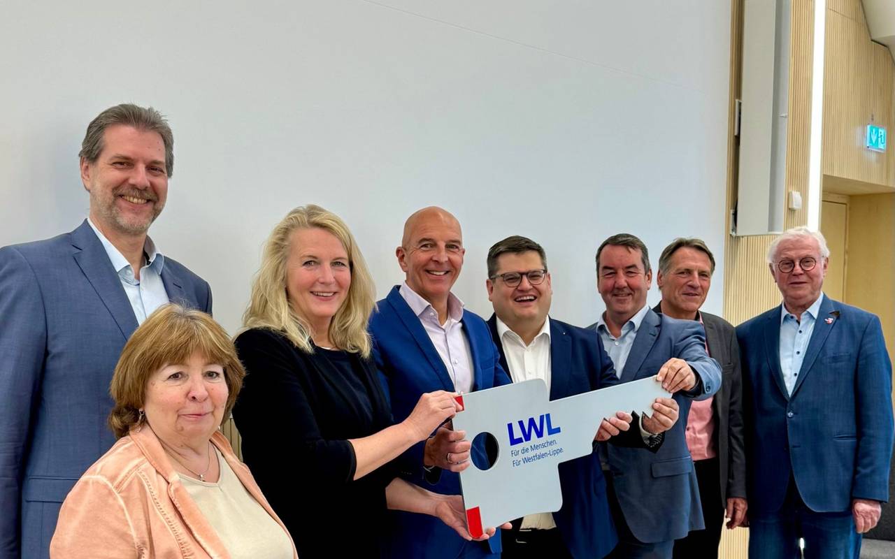 Acht erwachsene Menschen mit einem überdimensionalen Schlüssel