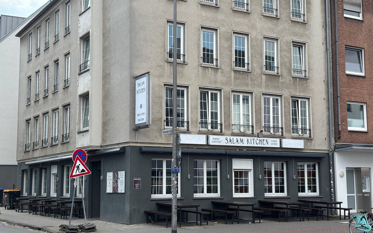 Ein Restaurant im unteren Bereich eines Wohnhauses. Es ist in schwarz gestrichen. Auf einem Schild steht der Name des Restaurants: Salam Kitchen.