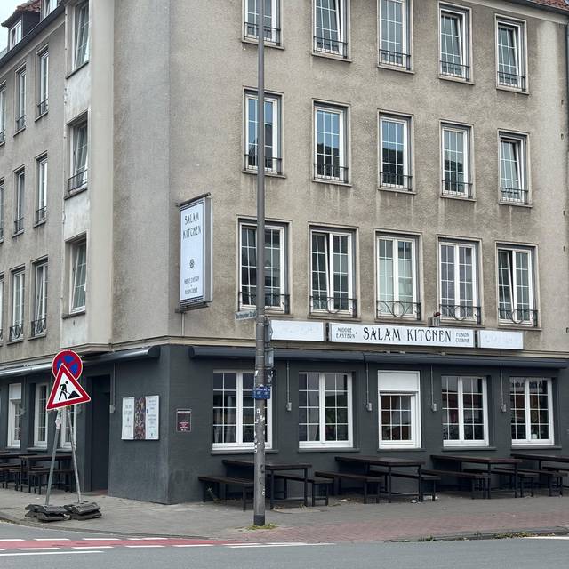 Ein Restaurant im unteren Bereich eines Wohnhauses. Es ist in schwarz gestrichen. Auf einem Schild steht der Name des Restaurants: Salam Kitchen.
