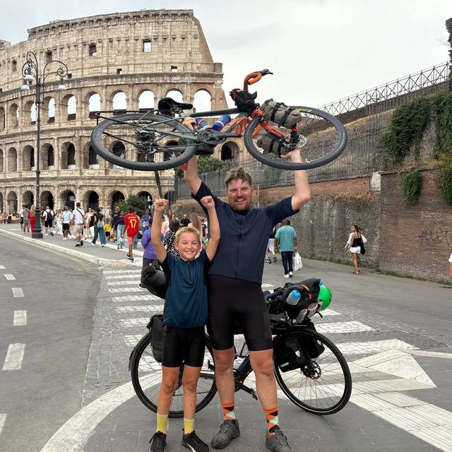 Jakob und Christian recken vor dem Kolosseum in Rom ihre Räder in die Höhe.