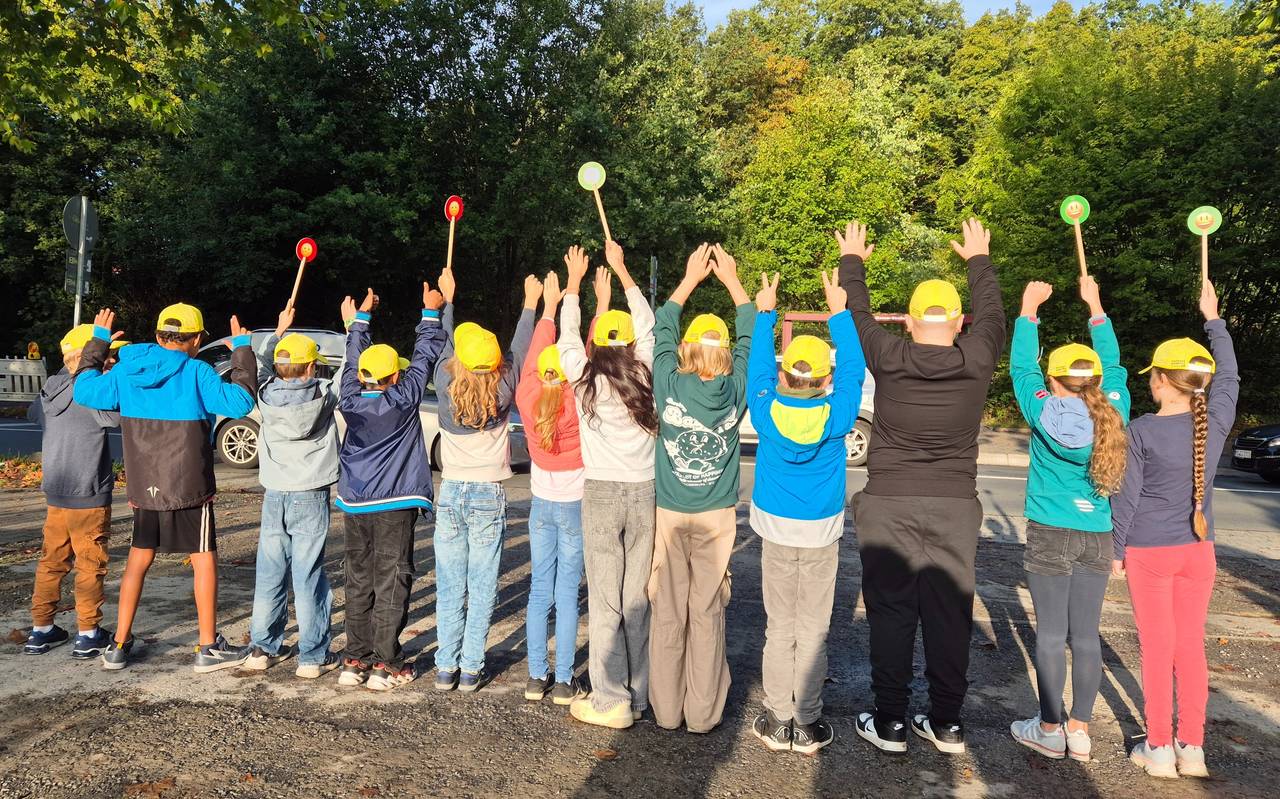 Viele Kinder mit gelben Käppis stehen nebeneinander und recken ihre Arme in die Luft.
