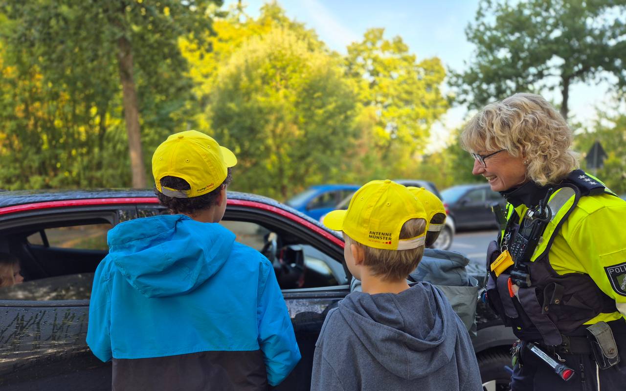 Zwei Kinder und eine Polizistin stehen an einem Auto.