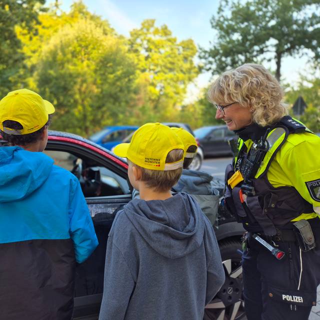 Zwei Kinder und eine Polizistin stehen an einem Auto.