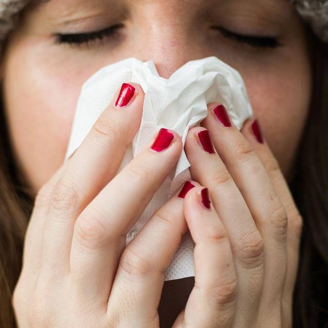 Frau hält sich ein Papiertaschentuch vor das Gesicht