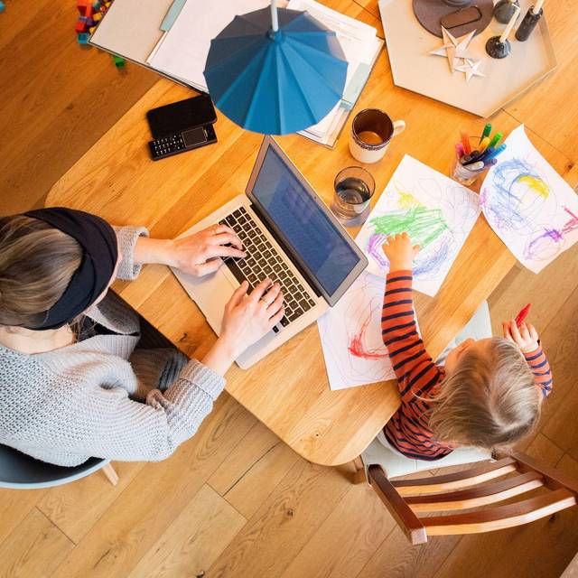 Eine Frau arbeitetneben ihrem Kind am Laptop