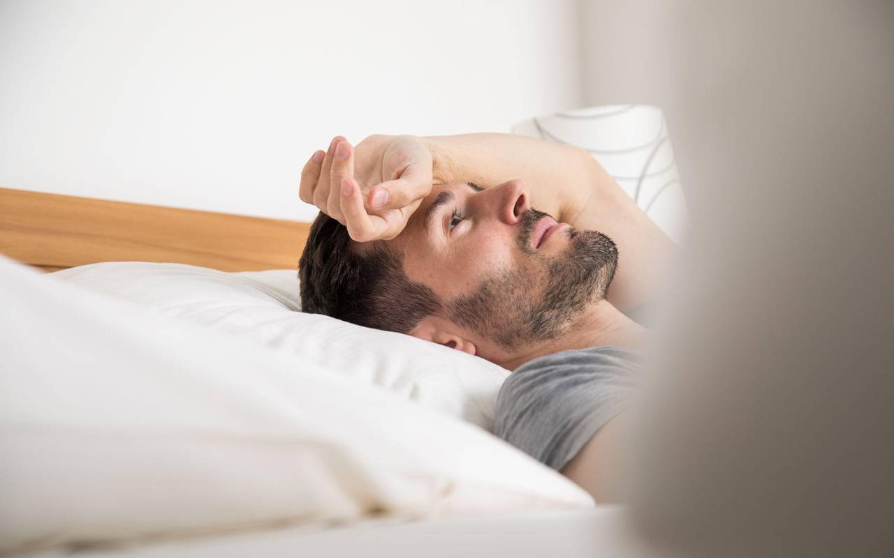 Mann liegt schlaflos im Bett