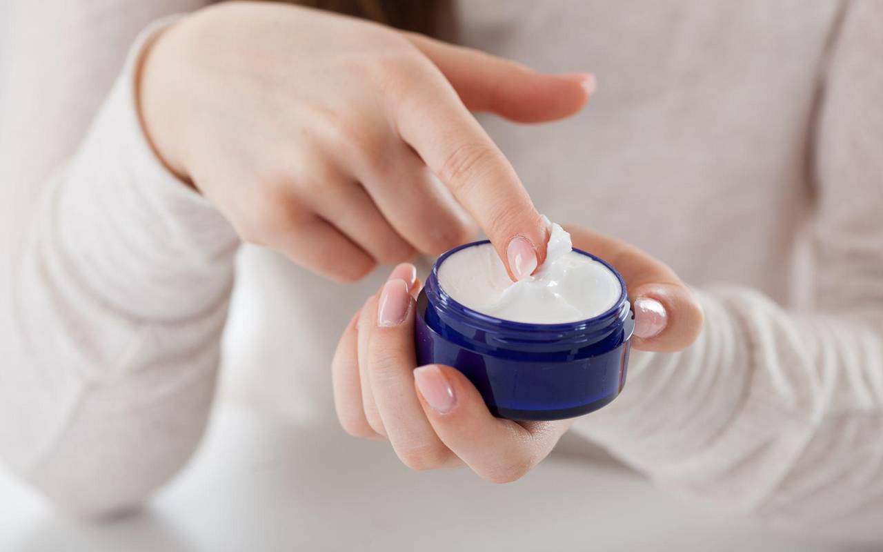 Eine Frau streicht mit dem Finger durch eine Cremedose