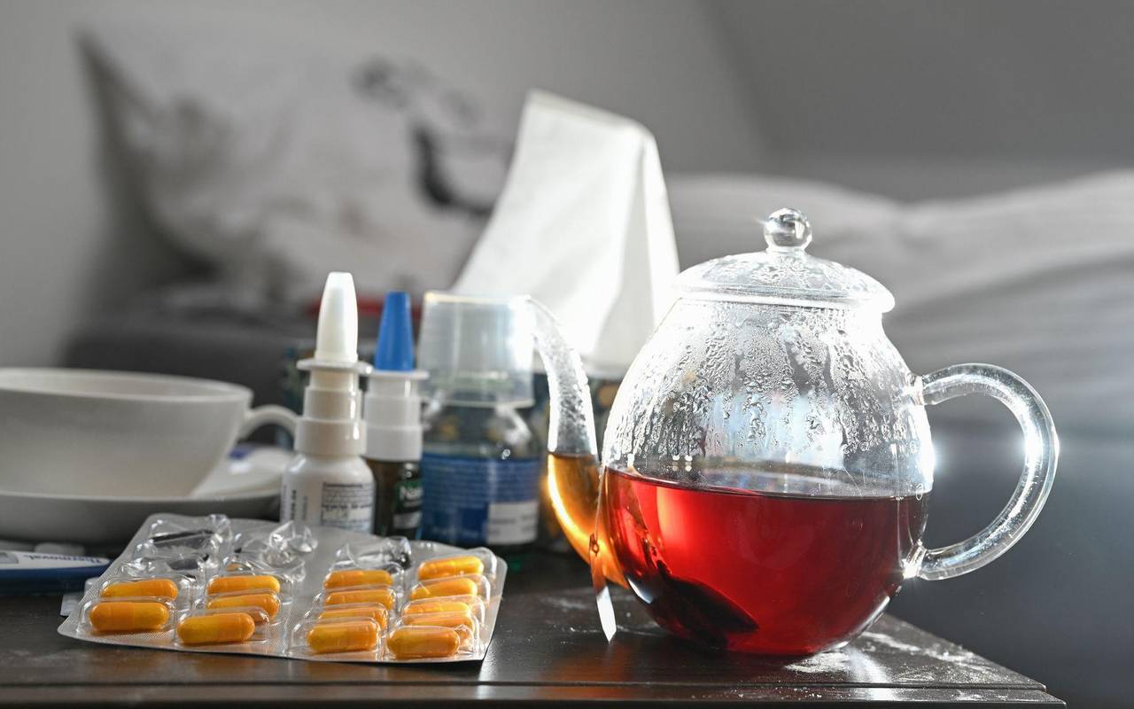 Medikamente und eine Kanne Tee auf einem Nachttisch