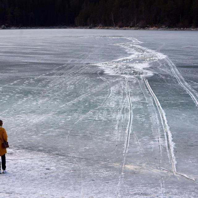 Eine Frau steht am zugefrorenem See nahe einer Einbruchstelle