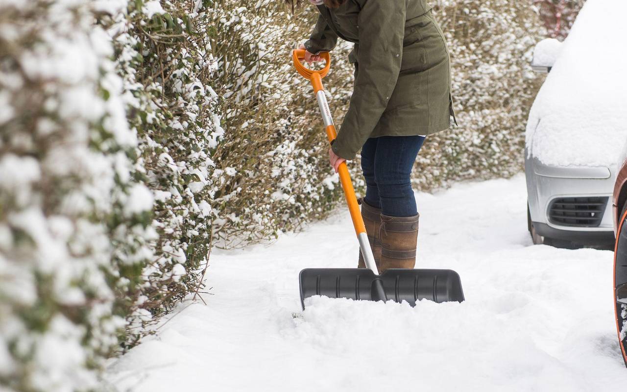 Eine Frau schippt Schnee auf dem Gehweg vor ihrem Haus