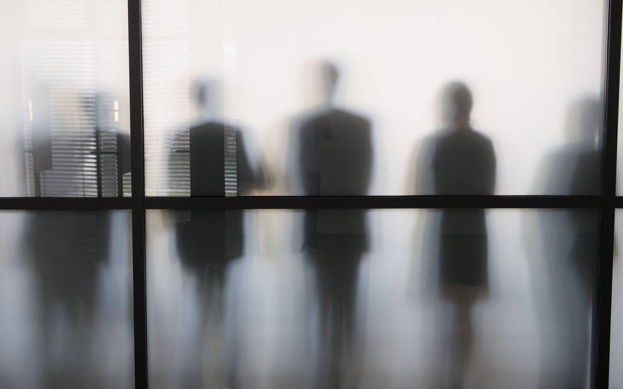 Personen stehen hinter eine Glasscheibe in einem Büro