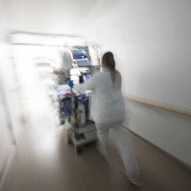 Pflegerin fährt eine Intensivpatientin durch denGang einer Klinik