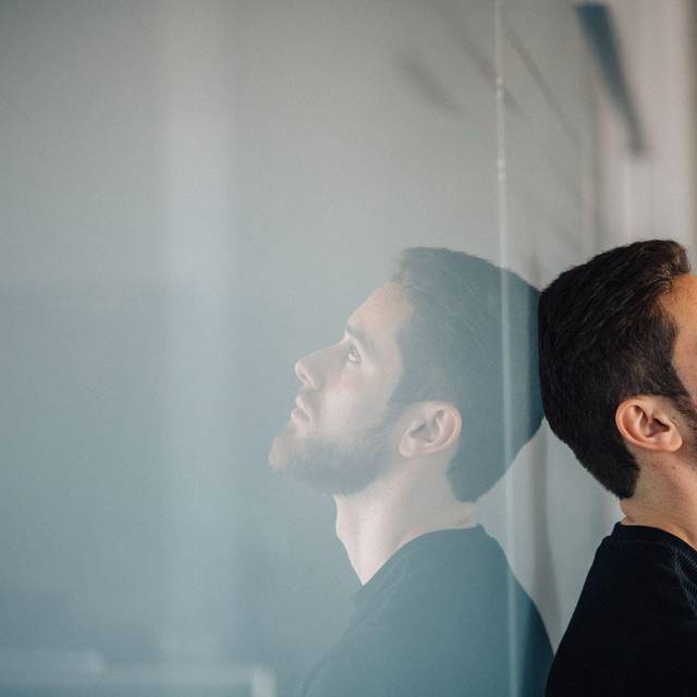 Ein junger Mann lehnt nachdenklich an einer Glaswand