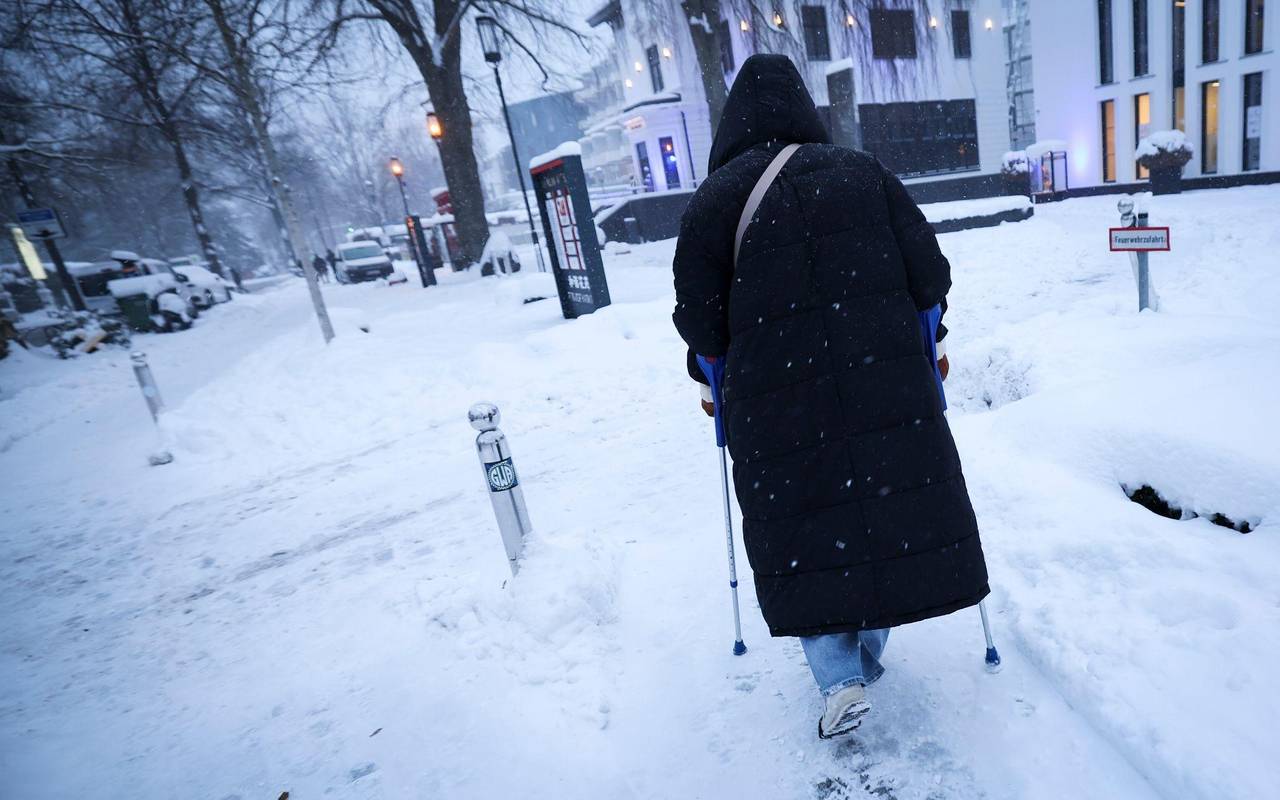 Ein Frau geht auf Eis mit Krücken und Spikes unter ihren Schuhen