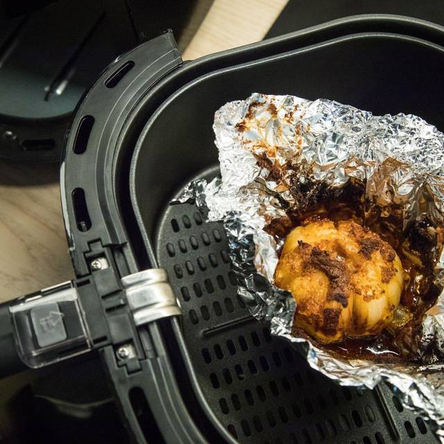 Eine in Alufolie gewickelte Zwiebel liegt in einem Airfryer
