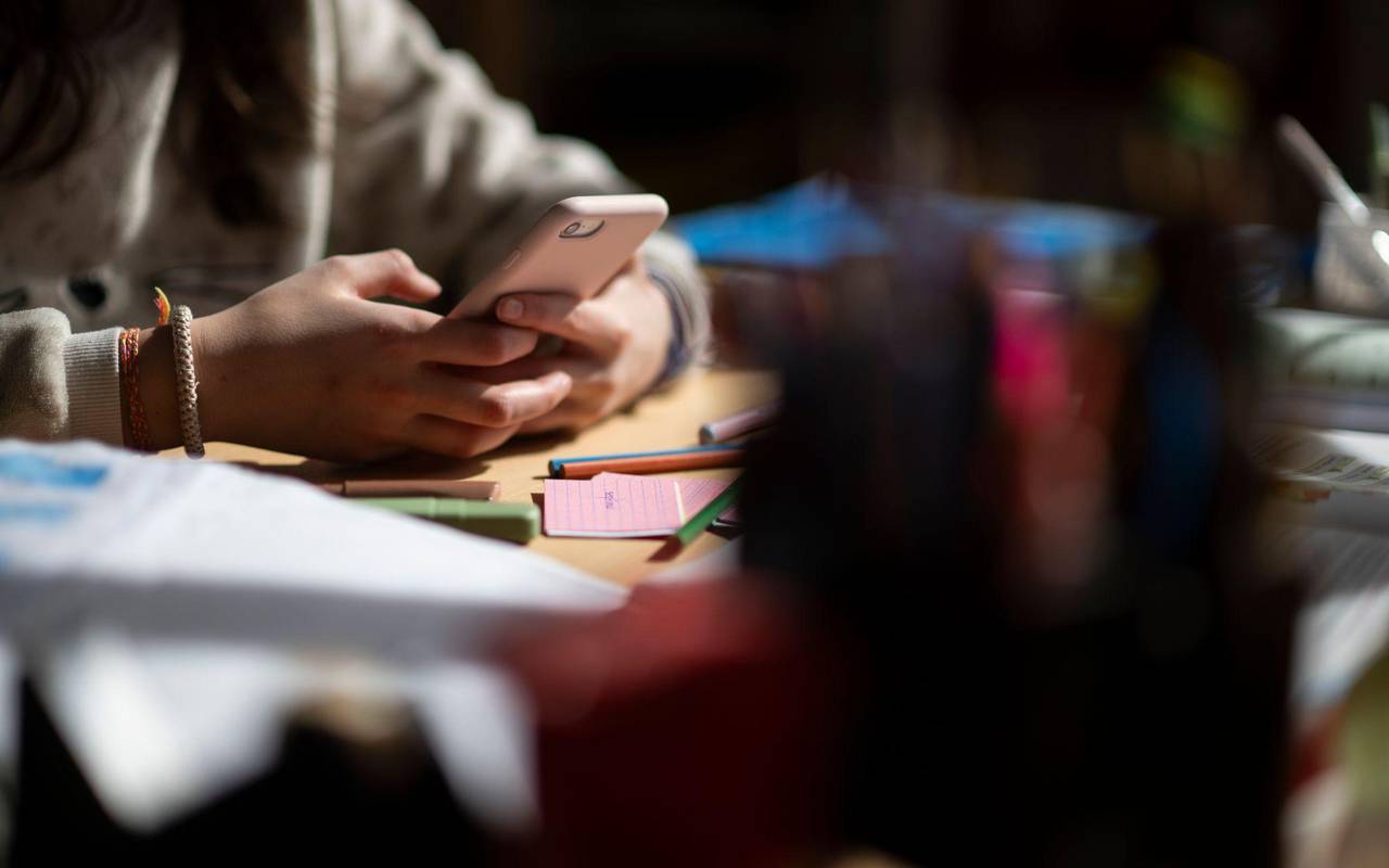 Eine Jugendliche sitzt mit Smartphone an einem Schreibtisch