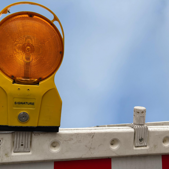 Eine Baustellenabsperrung mit orangenem Warnlicht vor blauem Himmel.