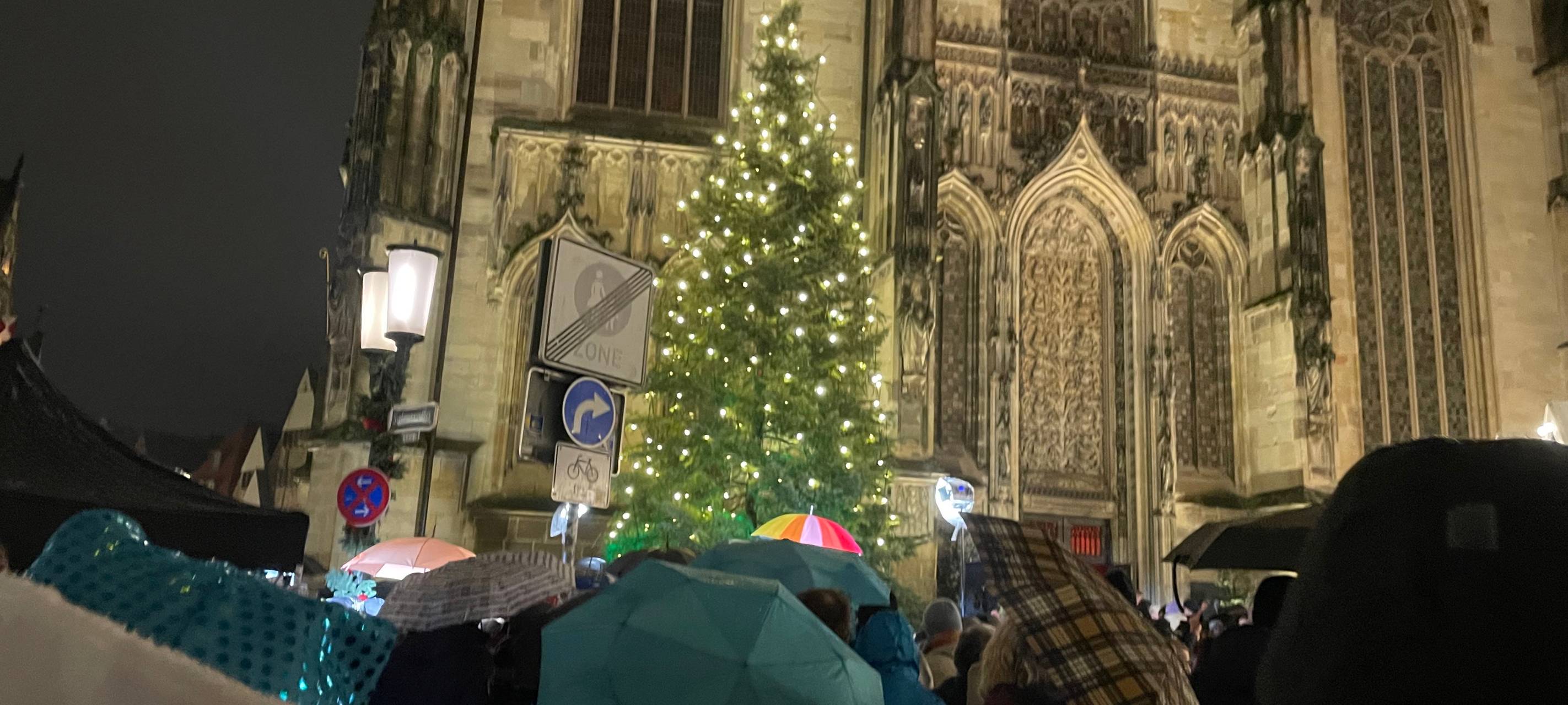 Vor der Lambertikirche steht eine Tanne. Sie ist mit einer leuchtenden Lichterkette geschmückt.