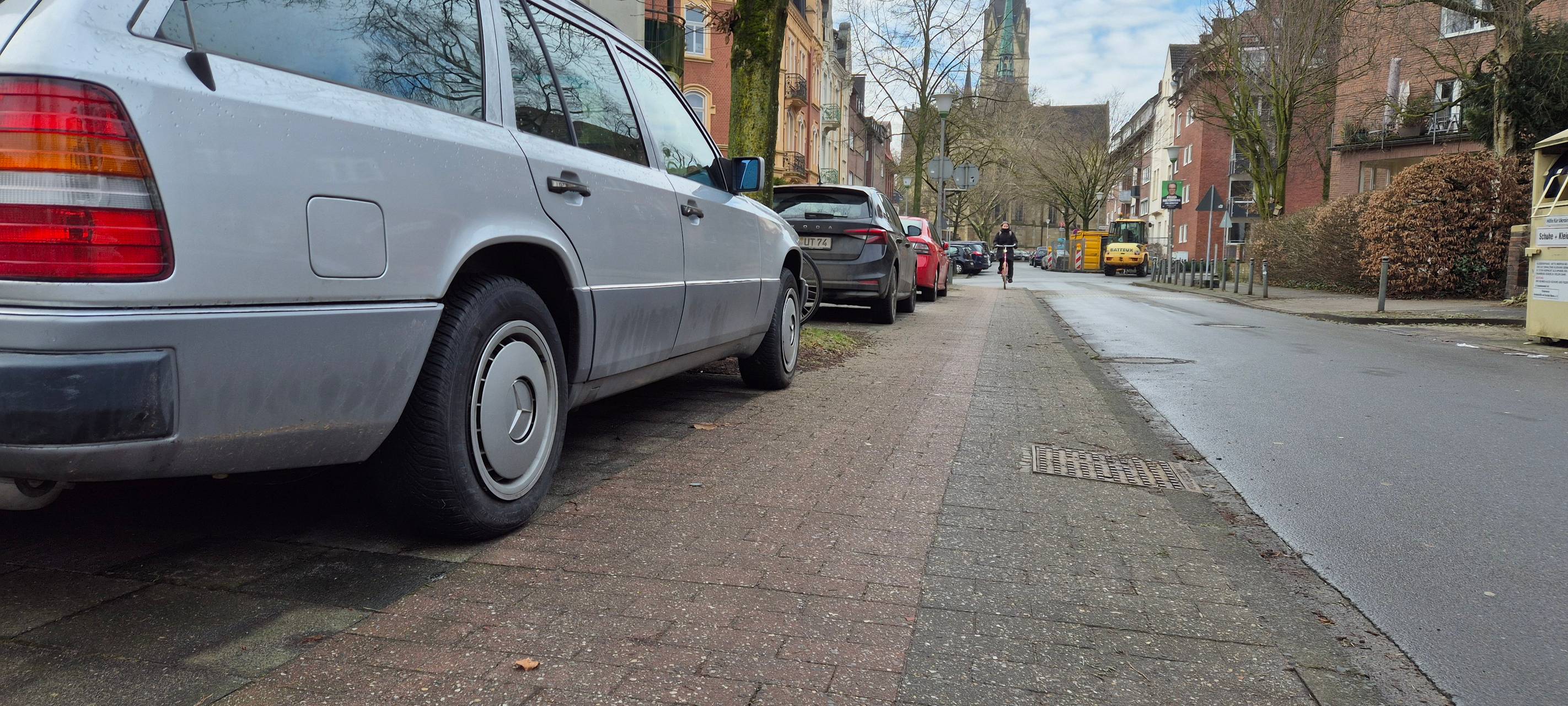 Auf dem Gehweg an einer Straße steht ein geparktes Auto. Daneben ist nur noch wenig Platz für einen Radstreifen. Vom Gehweg selbst ist nichts zu sehen.