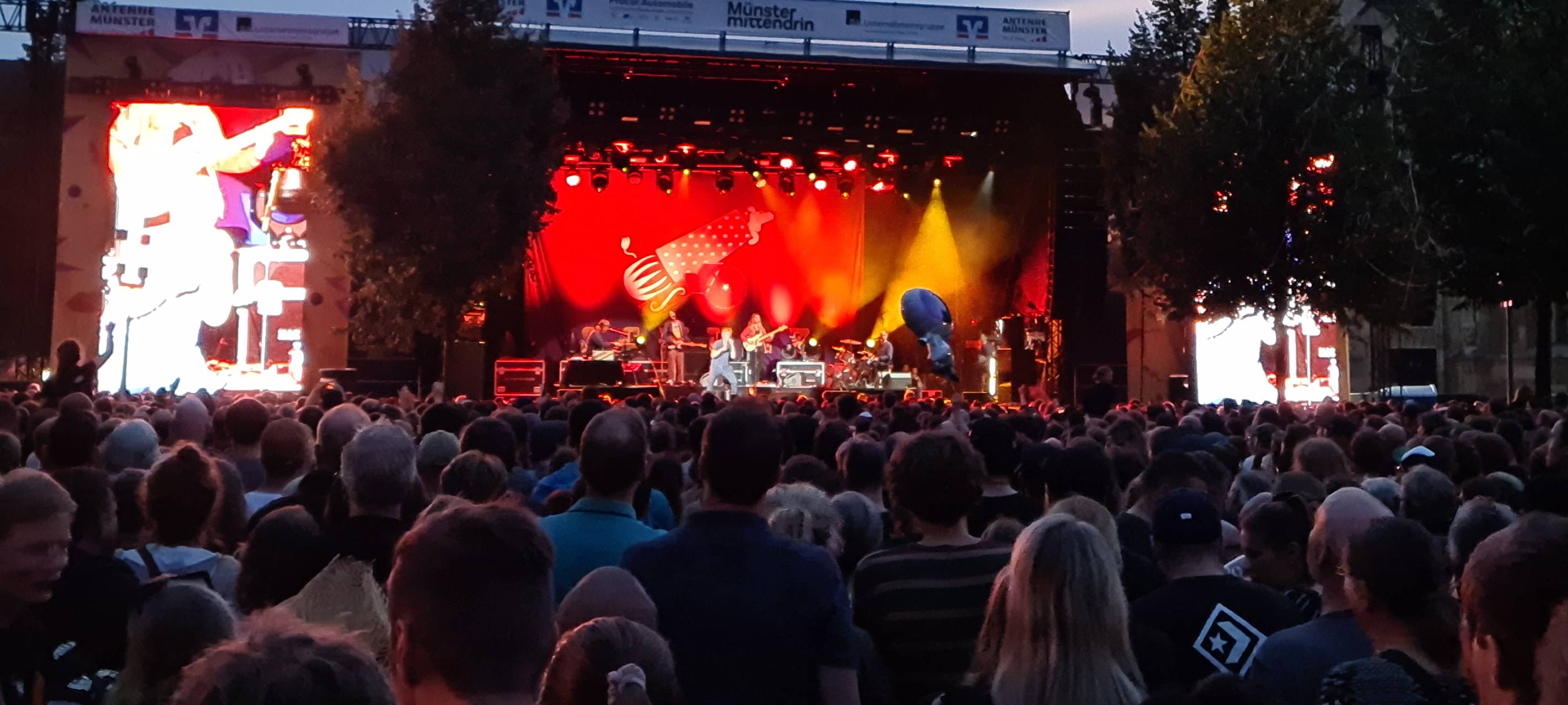 Eine Menge von Menschen steht mit dem Blick in Richtung einer Bühne. Die Bühne ist rot beleuchtet.