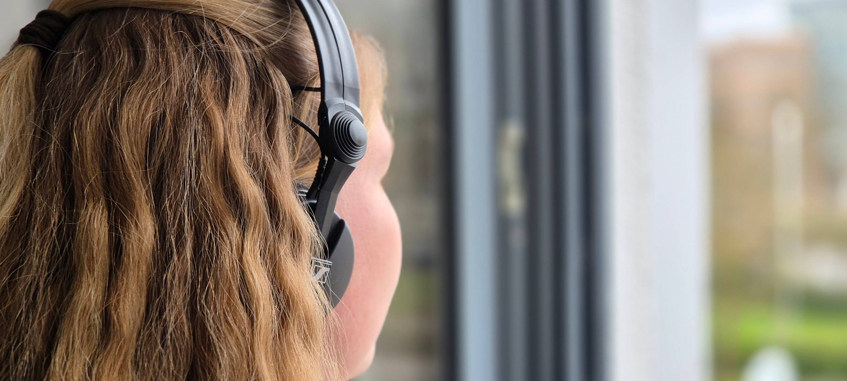 Eine junge Frau hört über Kopfhörer Musik und schaut dabei aus dem Fenster.
