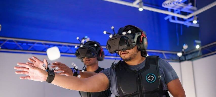 Zwei Menschen tragen eine große Virtual-Reality-Brille und schwarze Westen.