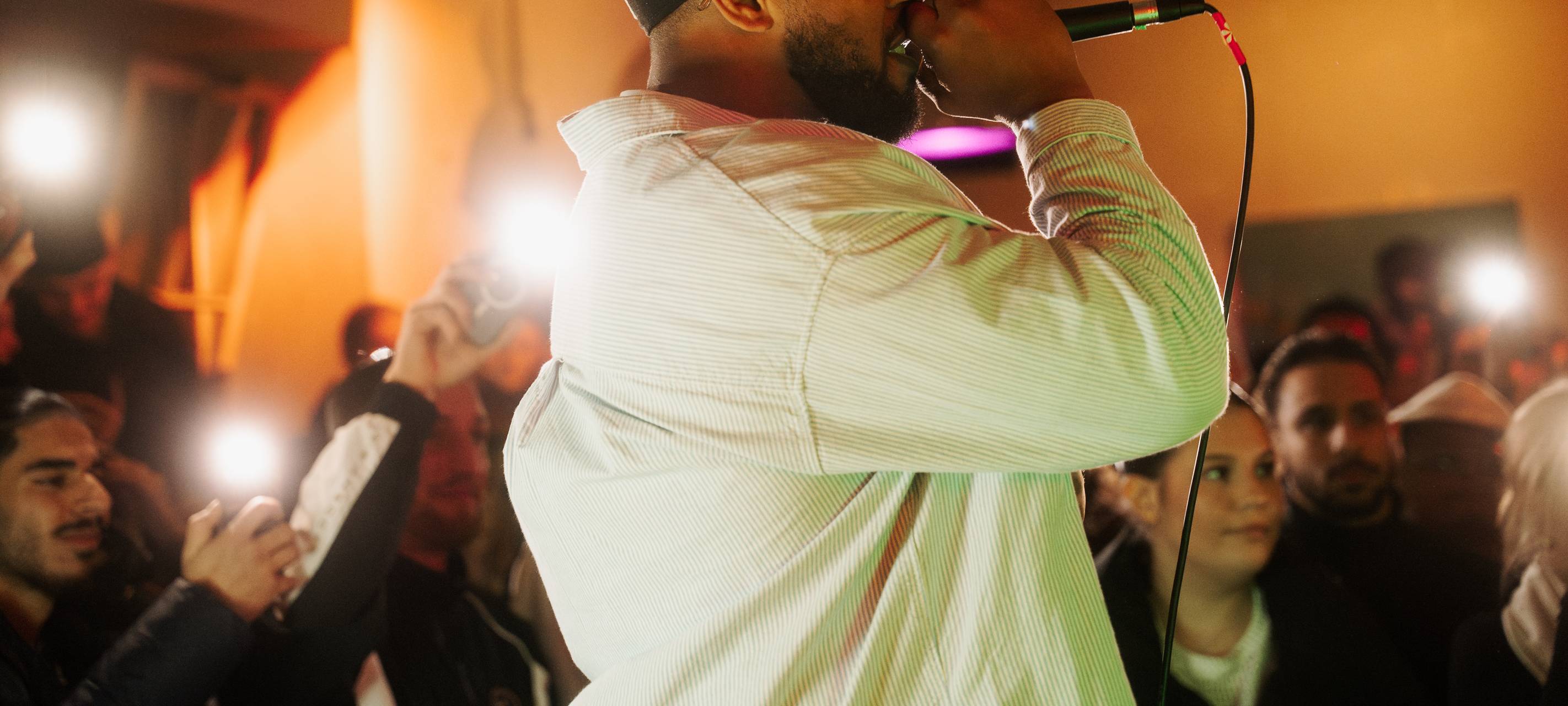 Der Sänger Frenci von der Seite. Er trägt eine Kappe und singt ins Mikrofon.