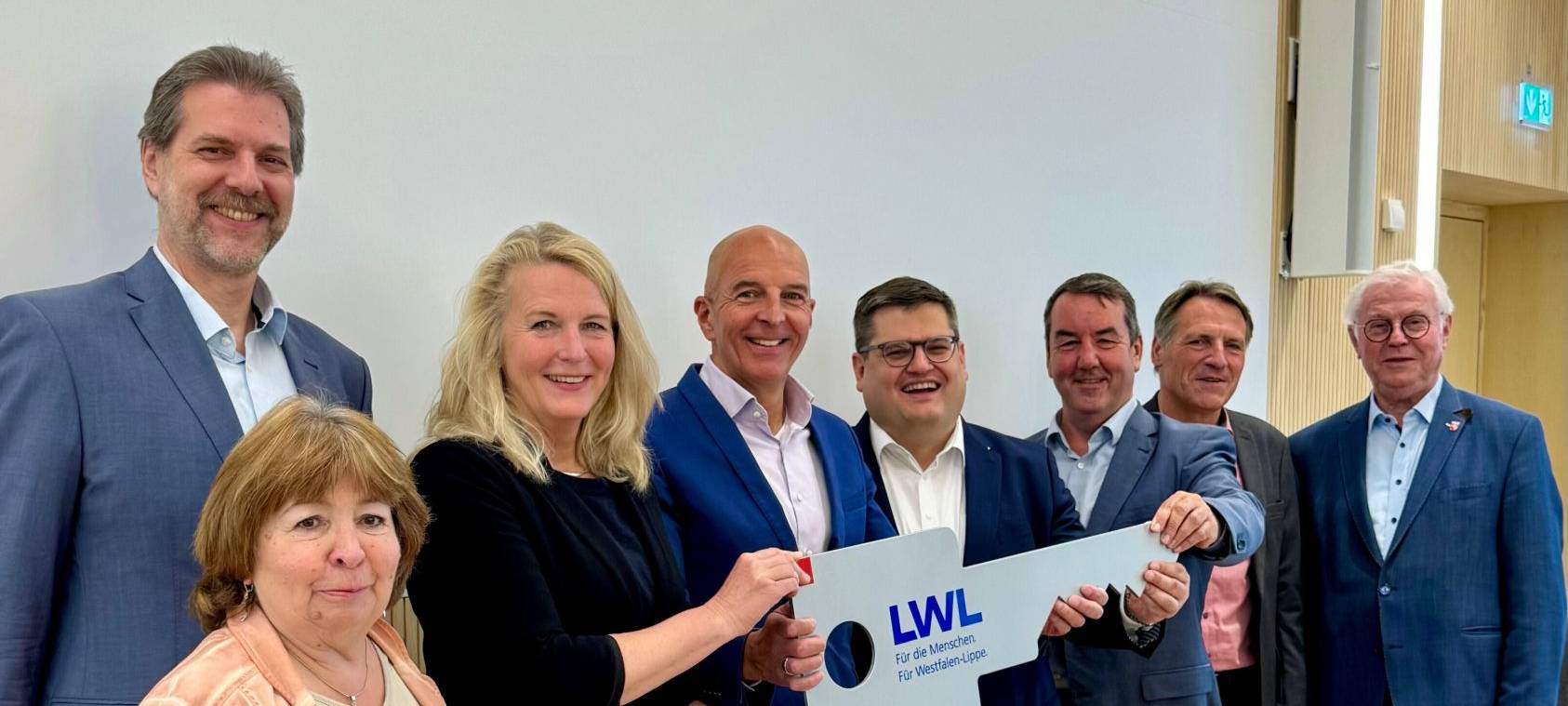 Acht erwachsene Menschen mit einem überdimensionalen Schlüssel