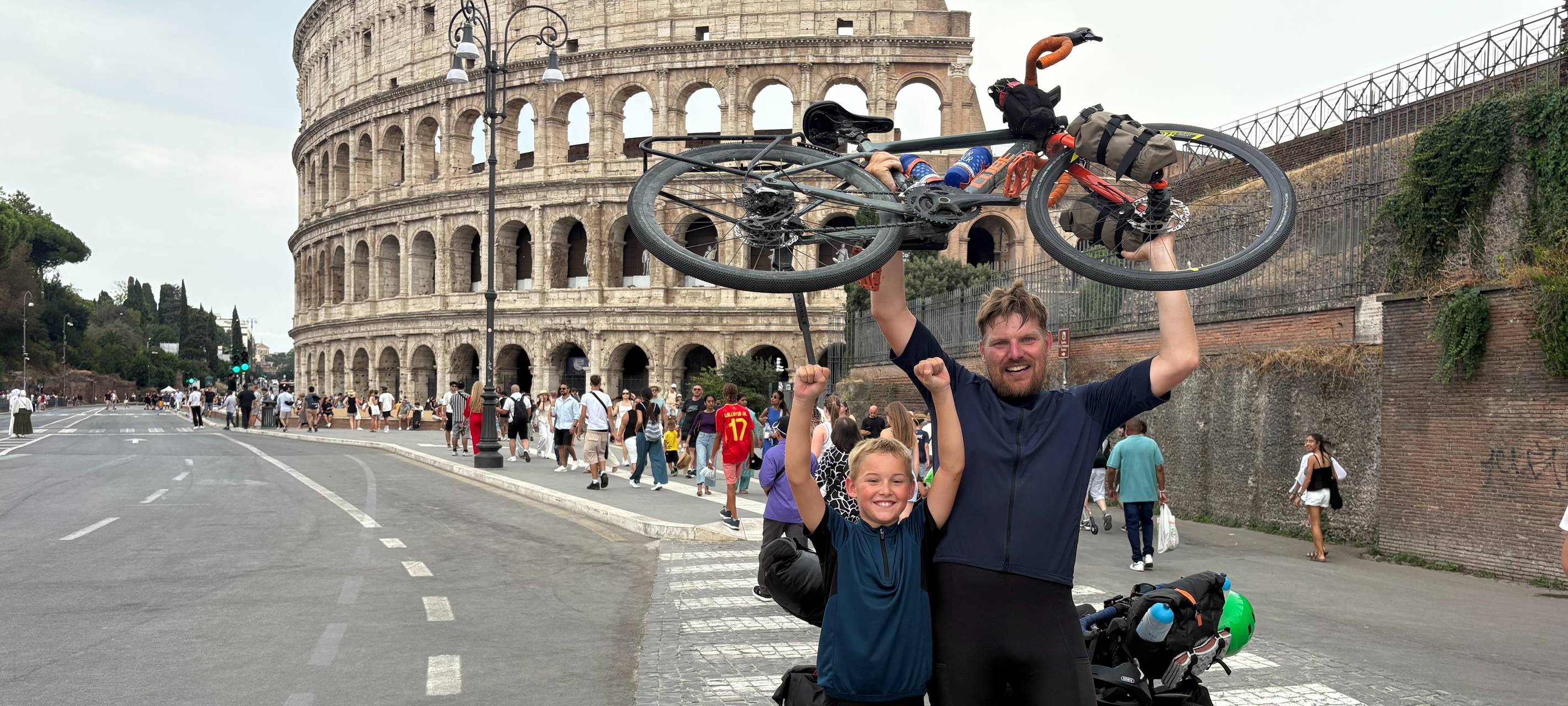 Jakob und Christian recken vor dem Kolosseum in Rom ihre Räder in die Höhe.