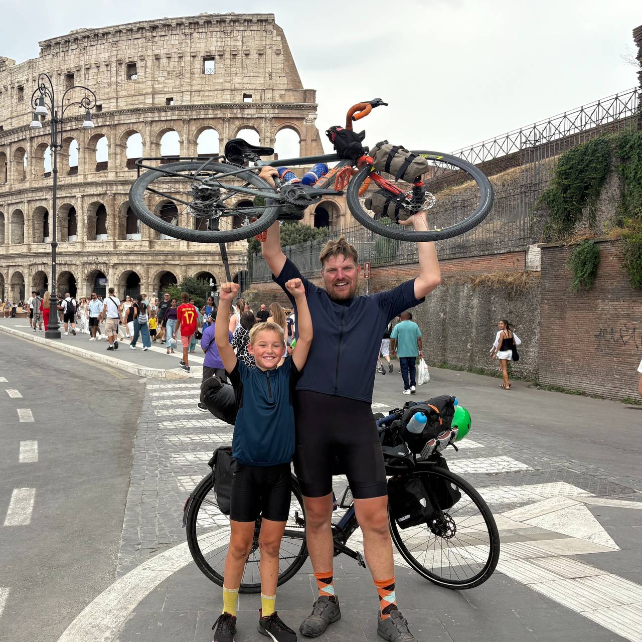 Jakob und Christian recken vor dem Kolosseum in Rom ihre Räder in die Höhe.