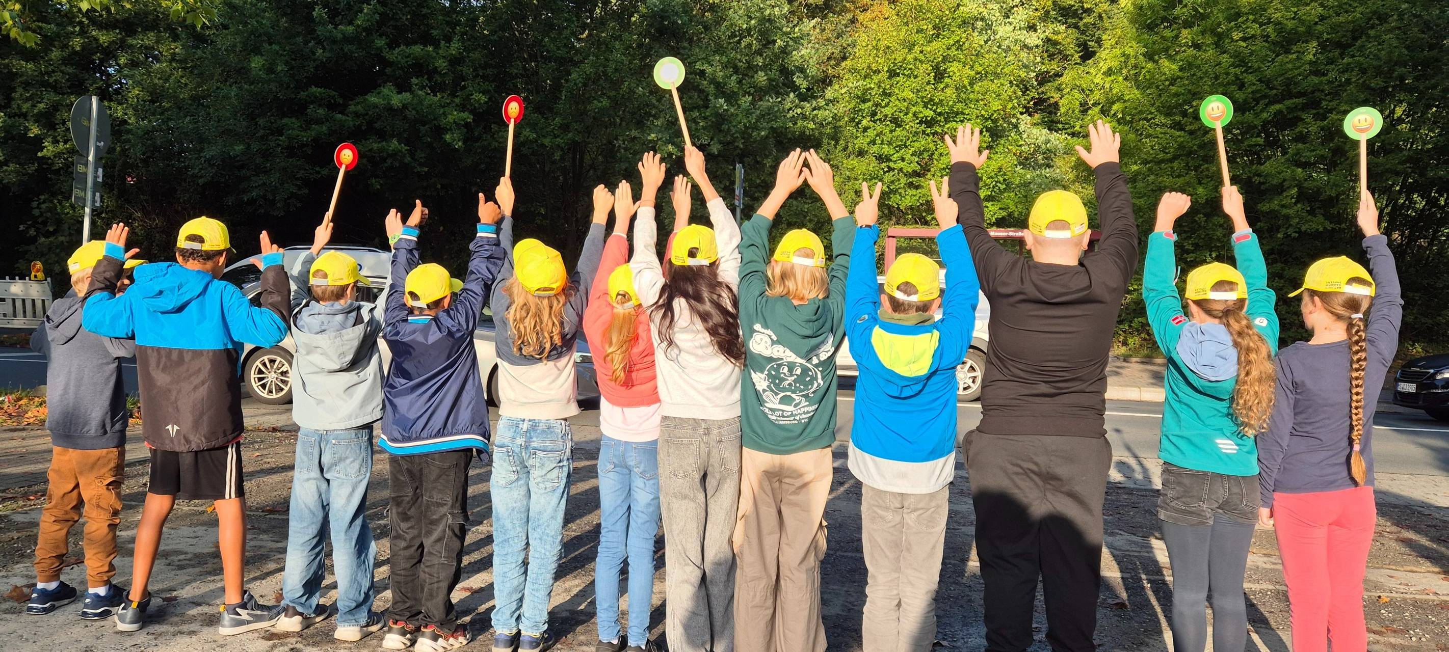 Viele Kinder mit gelben Käppis stehen nebeneinander und recken ihre Arme in die Luft.