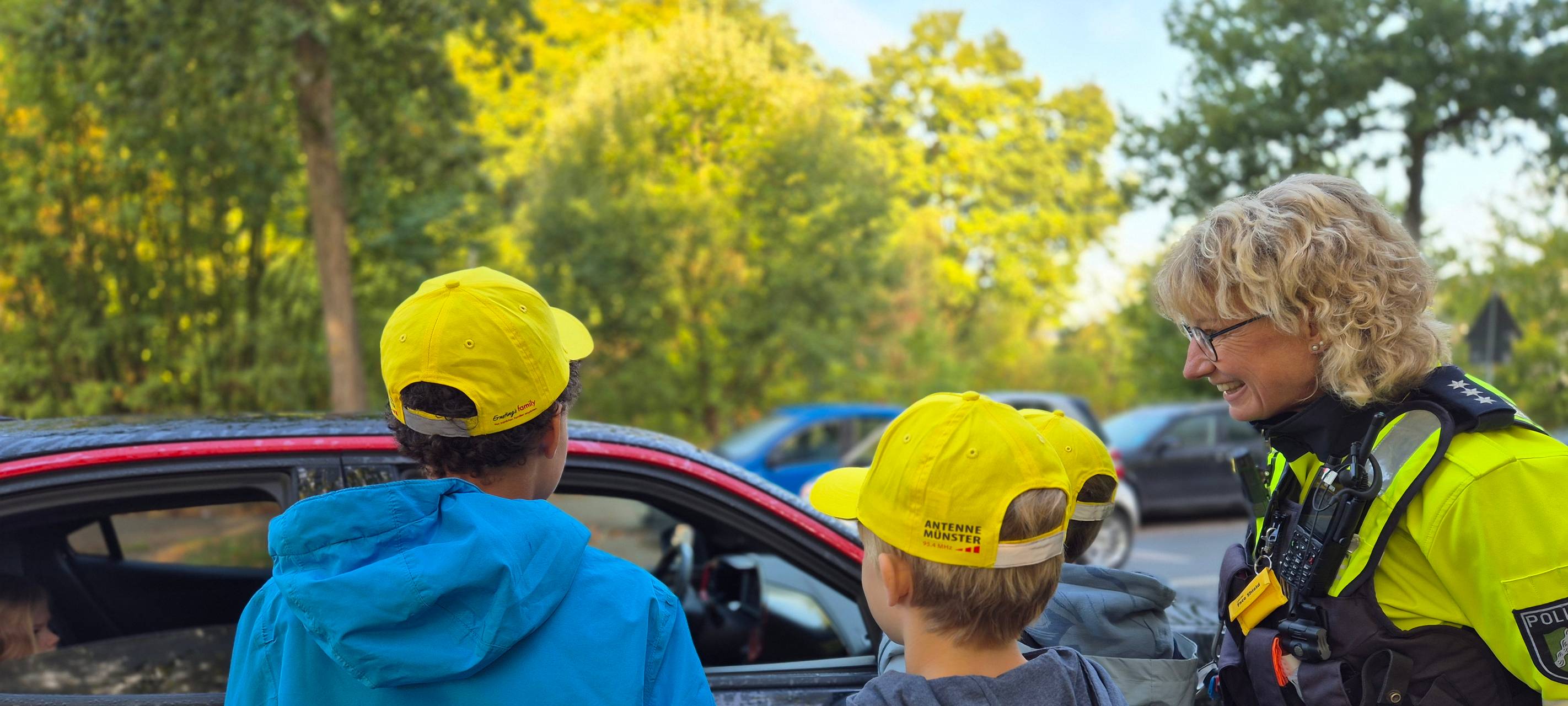 Zwei Kinder und eine Polizistin stehen an einem Auto.