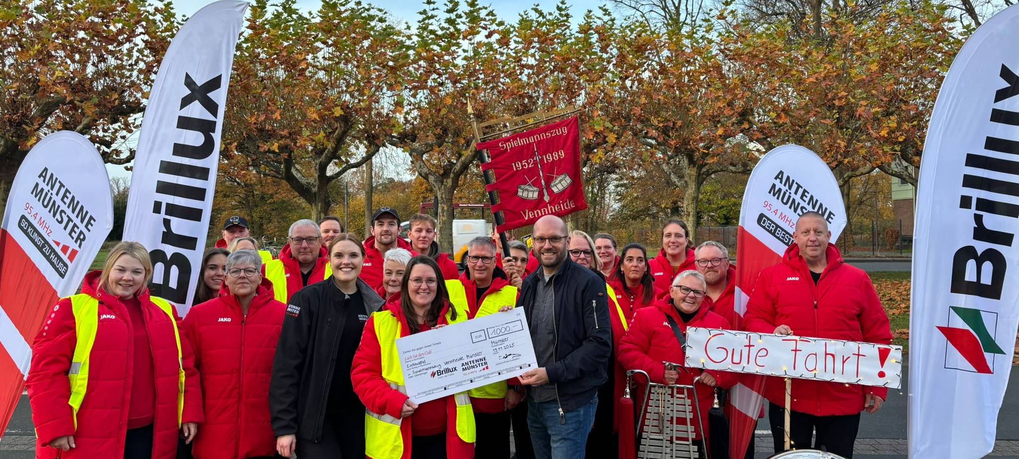 Malena Söhler aus der ANTENNE MÜNSTER-Morningshow "Zusammen wach" übergibt dem Spielmannszug Vennheide den Scheck über 1.000 Euro.