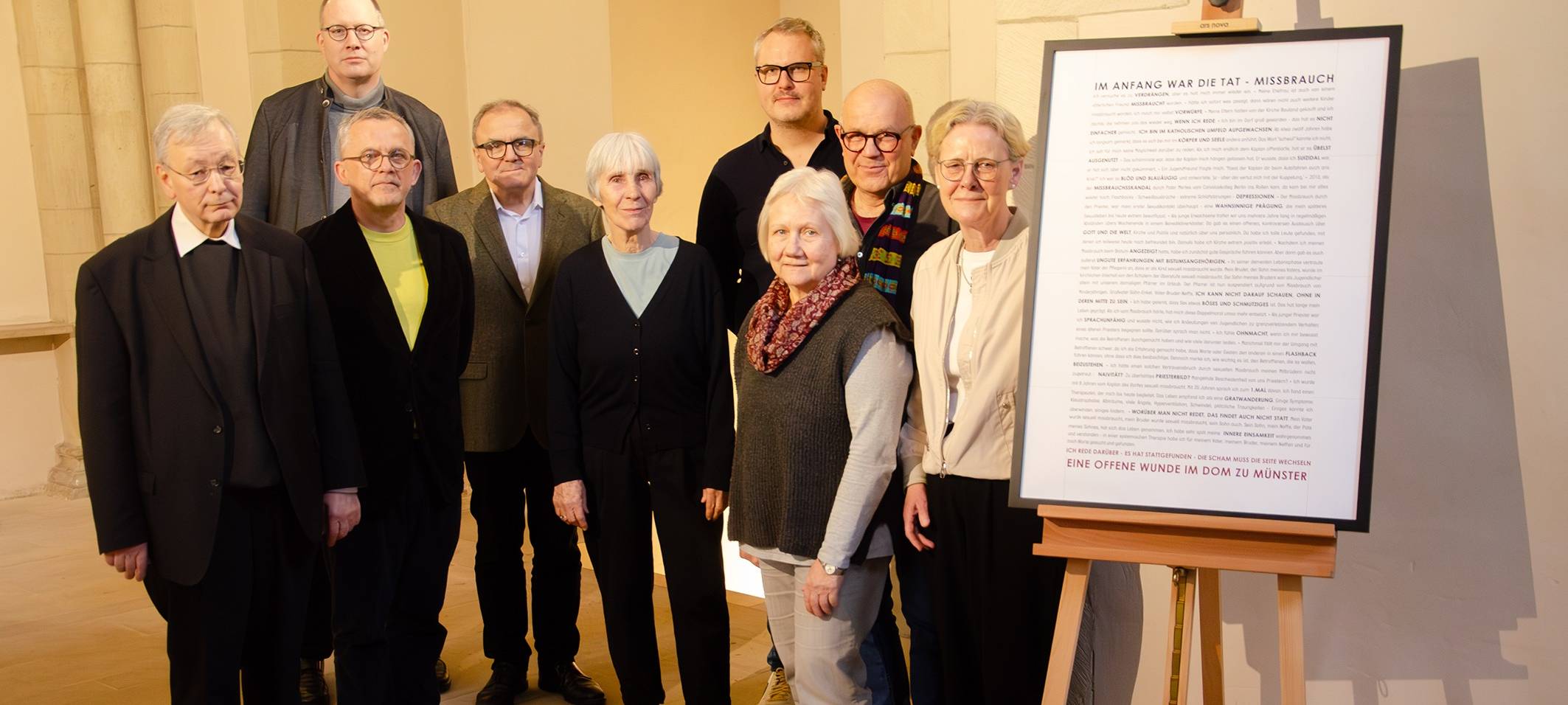 Das Foto zeigt die Arbeitsgruppe mit Dompropst Köppen neben dem Plakat am Eingang zur Bischofsgruft. Von links: Domkapitular Gerhard Theben, Domkapitular André Sühling, Christoph Achterkamp, Dompropst Hans-Bernd Köppen, Marianne Schmid, Bastian Weisweiler, Brigitte Lehmann, Ulrich Schulze Bertelsbeck und Anette Brachthäuser.
