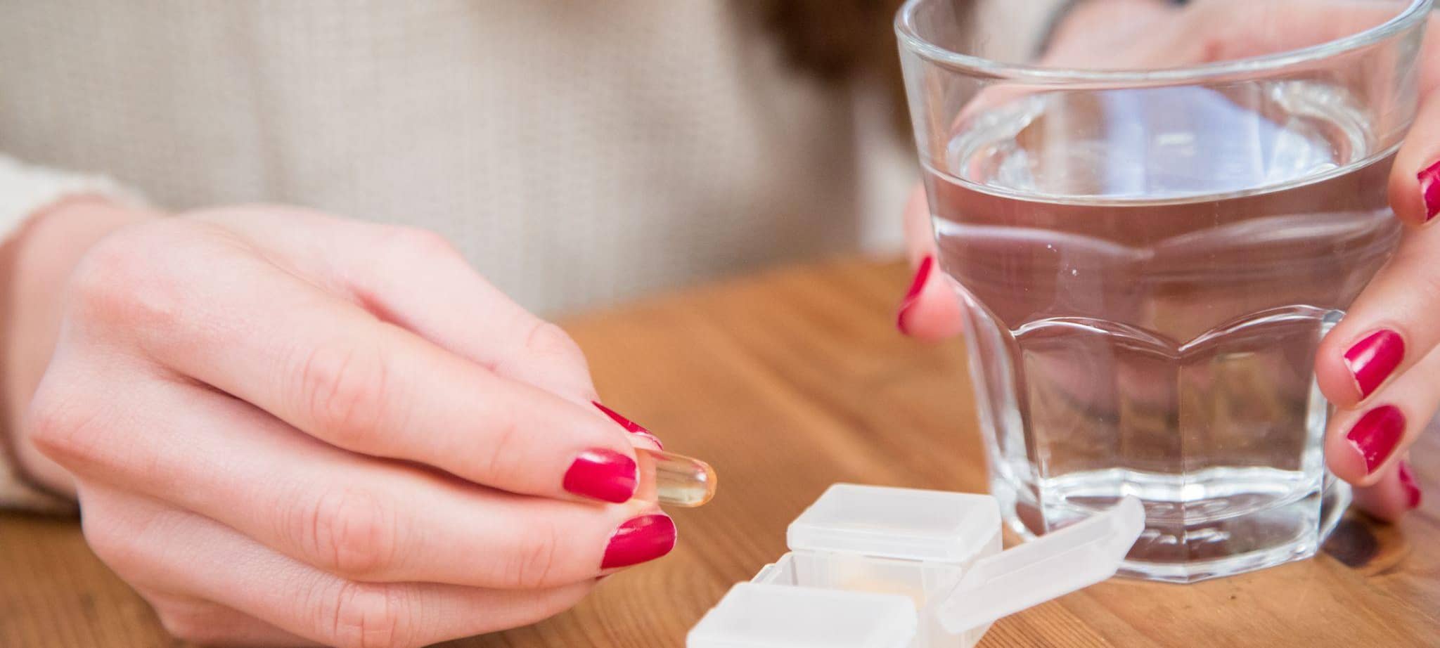 Eine Frau hält eine Kapsel und ein Glas Wasser in der Hand