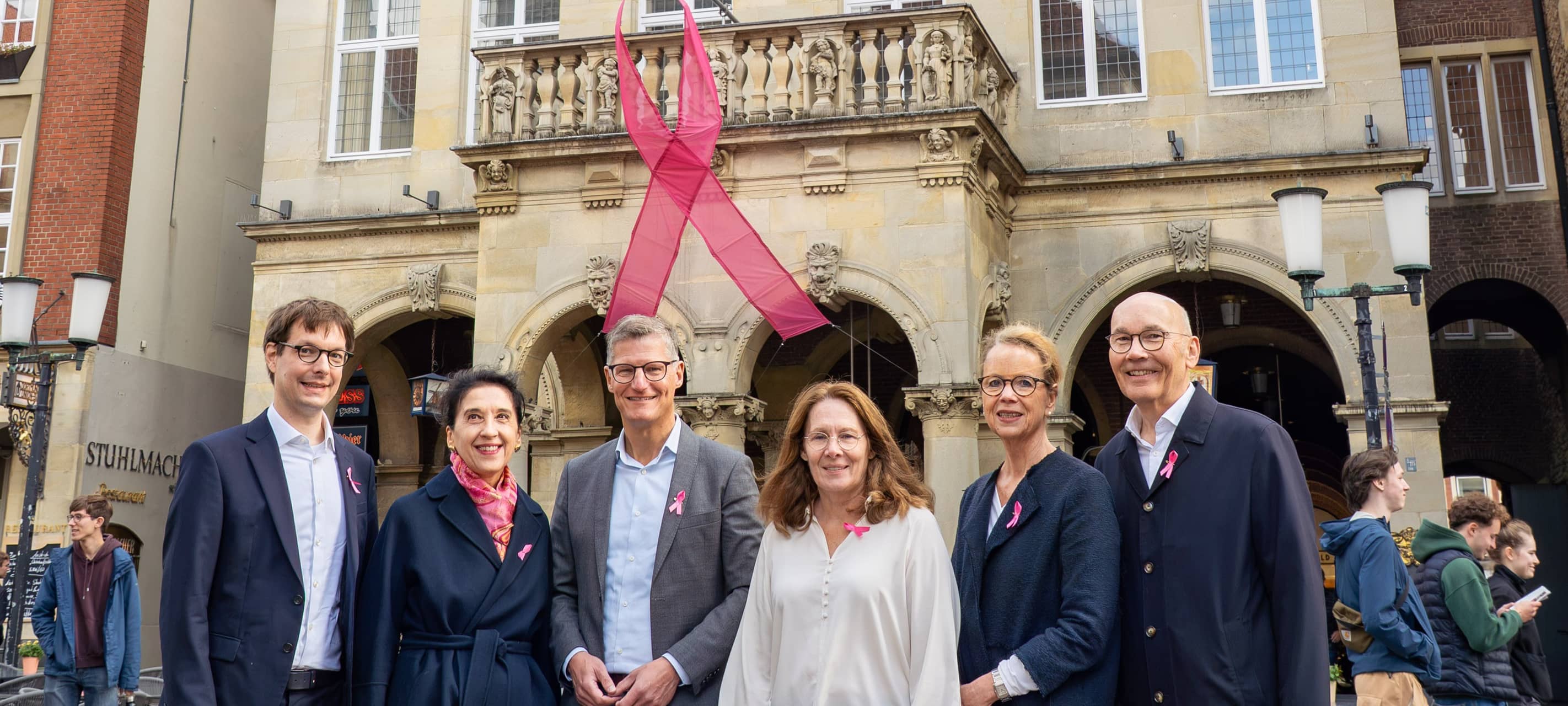 „Pink Ribbon“ am Stadtweinhaus auf dem Prinzipalmarkt: Oberbürgermeister Tilman Fuchs (3.v.l.) präsentierte am Donnerstag (8. Oktober) das Symbol der Brustkrebsfrüherkennung gemeinsam mit Prof. Dr. Walter Heindel (rechts), Claudia Verloh und Prof. Dr. Stefanie Weigel (links daneben) vom Referenzzentrum Mammographie Münster. Heindel und Weigel sind wie Dr. Matthias Burg (links) auch Programmverantwortliche der Referenz-Screening-Einheit Münster-Nord/Warendorf in der Königsstraße, was für die Ärztin Simona Spital (2.v.r.) in der Screening-Einheit Münster-Süd/Coesfeld am Clemenshospital gilt.