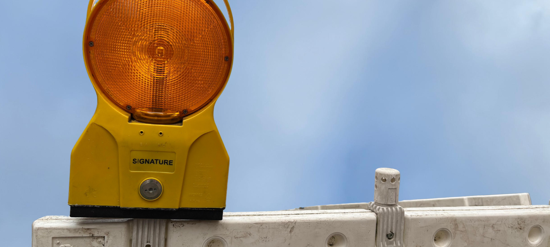 Eine Baustellenabsperrung mit orangenem Warnlicht vor blauem Himmel.