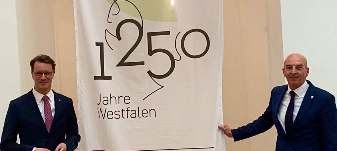 Auf der linken Seite steht Ministerpräsident Hendrik Wüst. Auf der anderen Seite steht der LWL-Direktor Dr. Georg Luhnemann. Zwischen ihnen hängt ein Banner. Darauf steht: 1250 Jahre Westfalen.