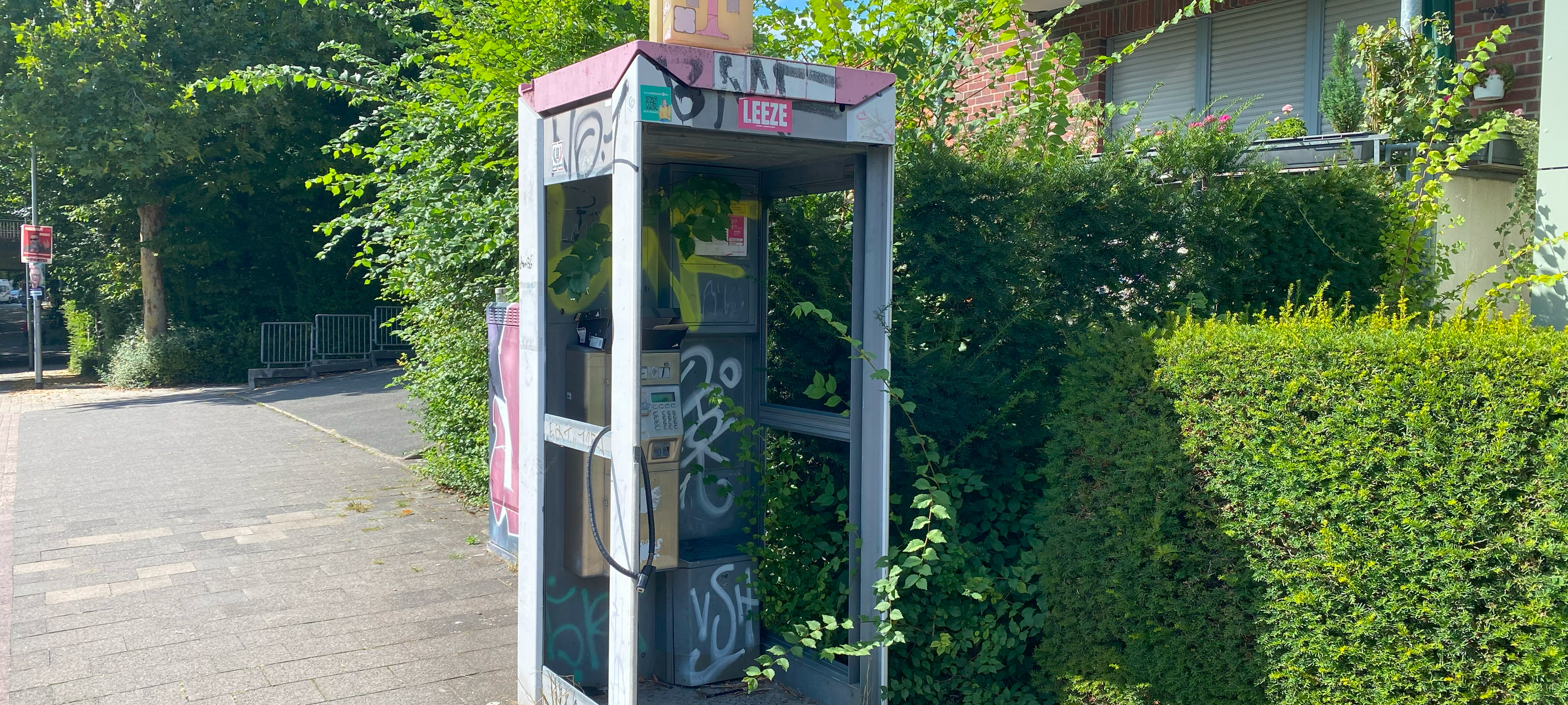 Das Foto zeigt eine mit Graffiti verschmierte, ungenutzte Telefonzelle.